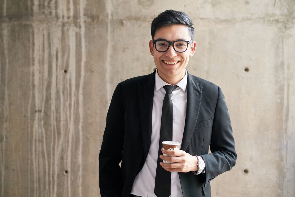 Business man smiling, standing with a cup of coffee.