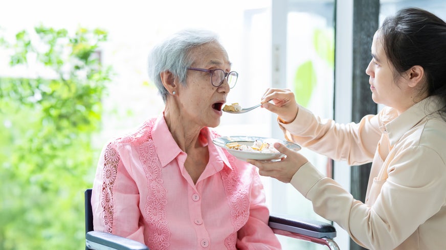 A woman is feeding an elderly woman in a wheelchair with a spoon.