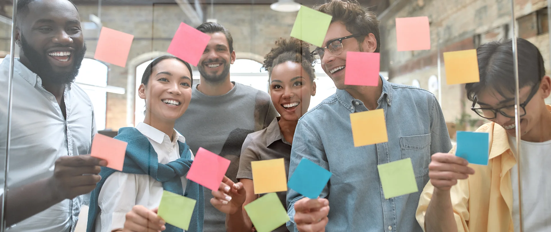 A group of people are holding sticky notes on a glass wall