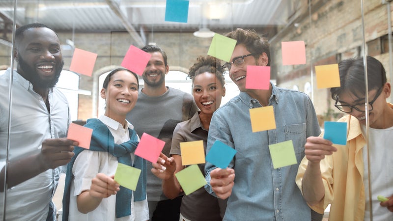 A group of people are holding sticky notes on a glass wall