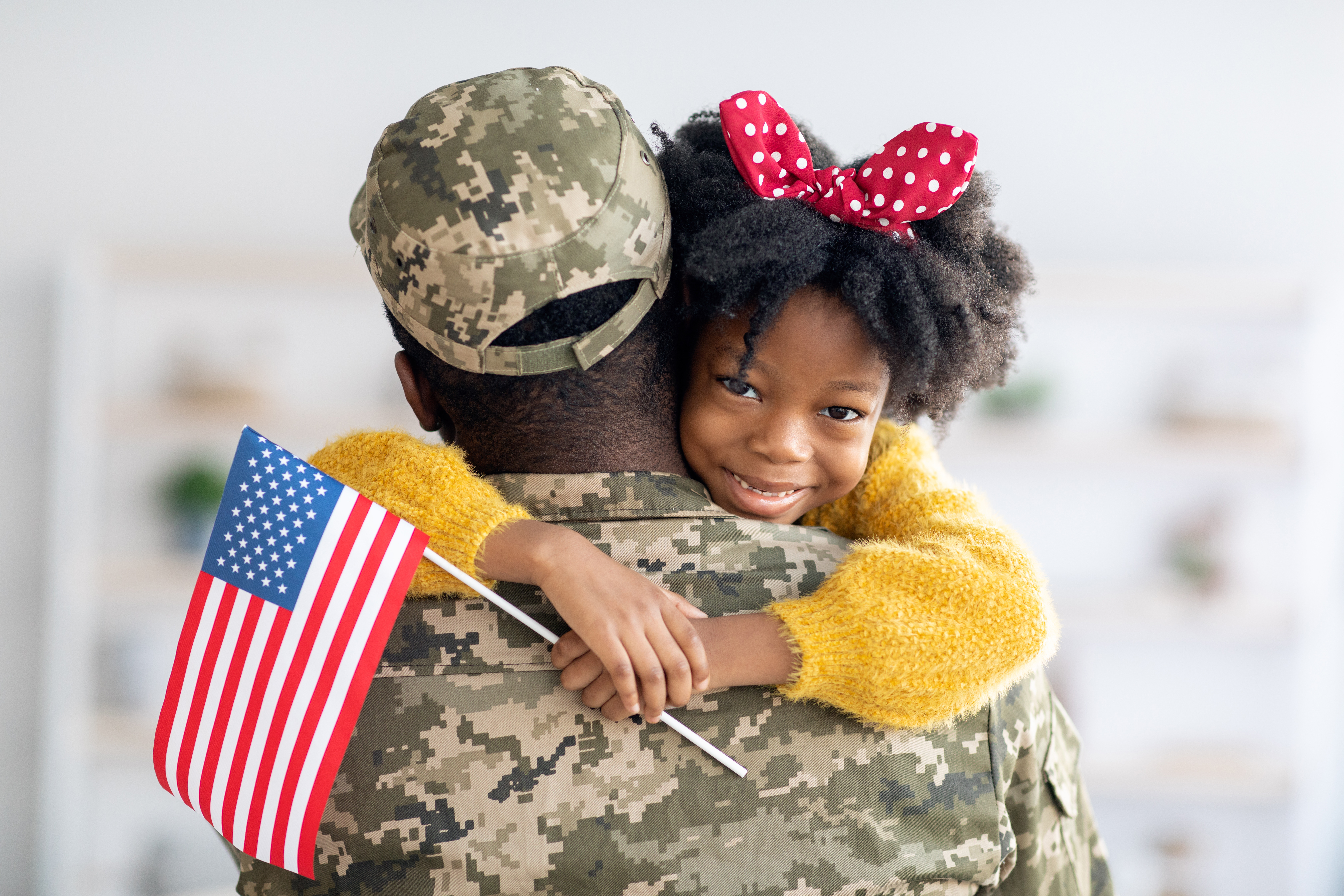 United States Veteran patient being hugged by a little girl holding a US flag.