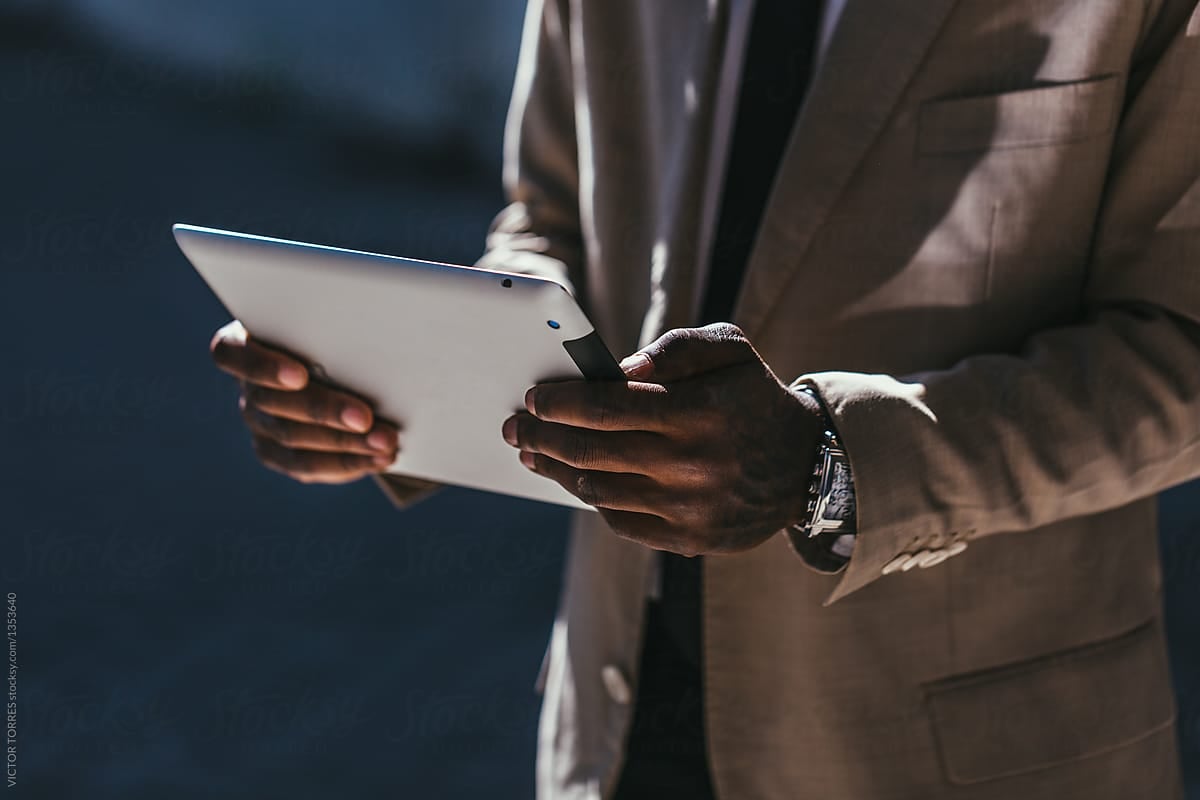 Man in a beige suit holding a tablet.