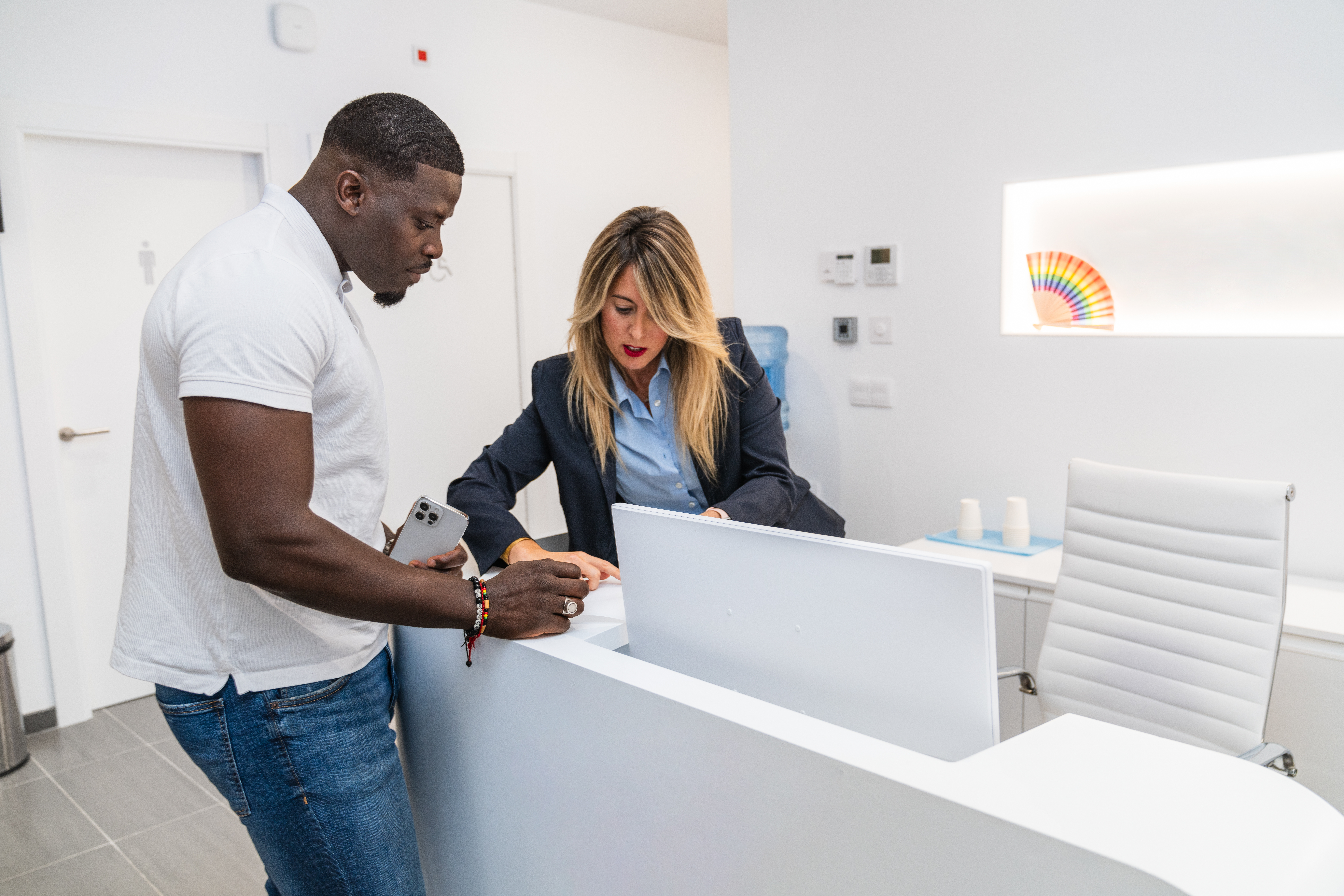 A man and a woman are standing at a reception desk in an office