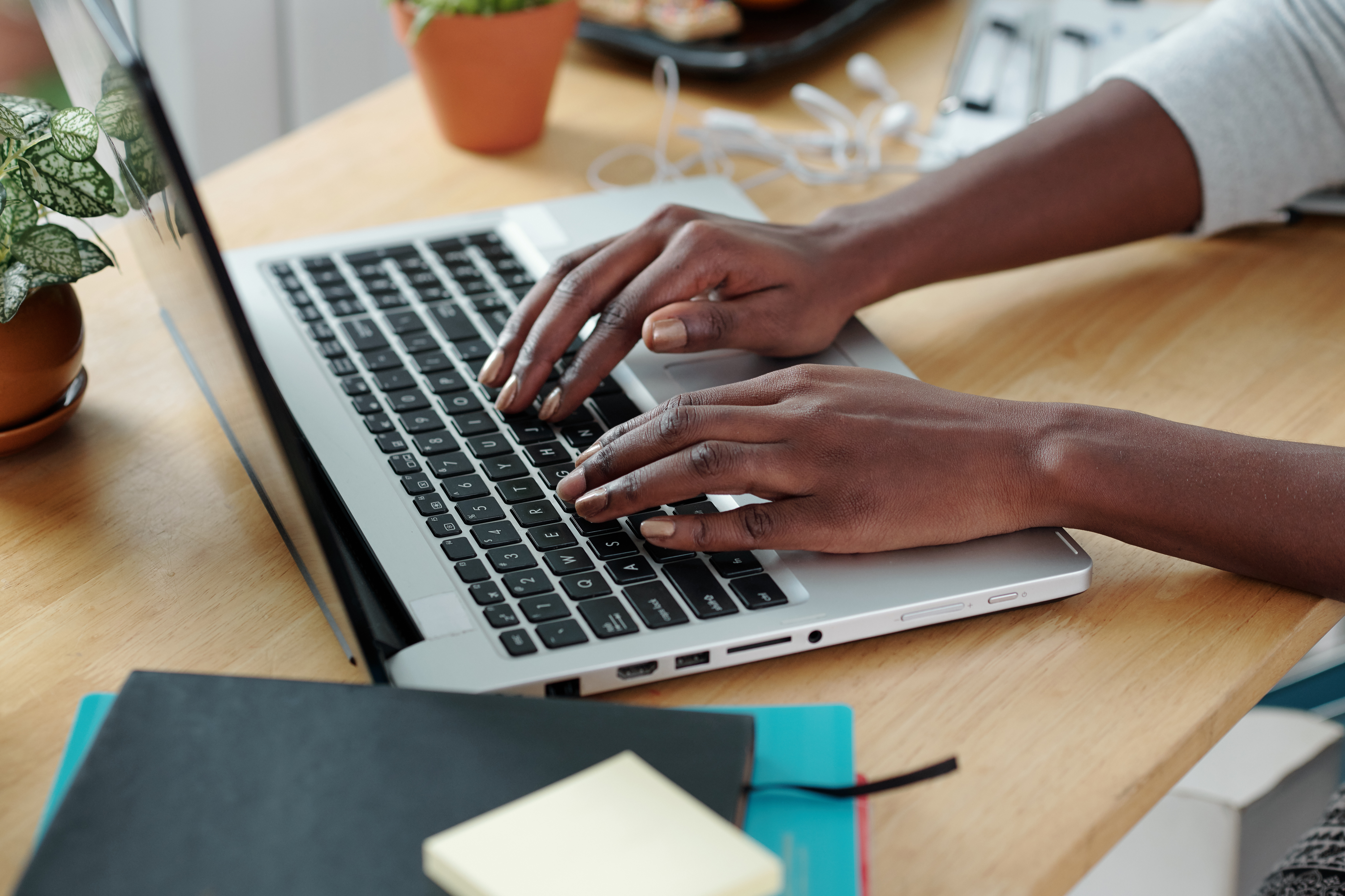 Person typing on a laptop at a desk with notebooks and plants