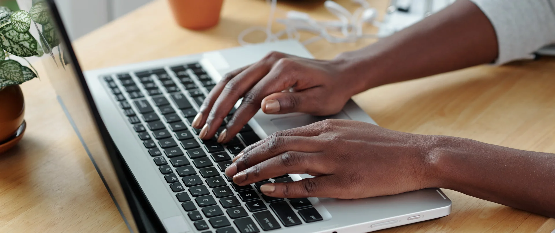 Person typing on a laptop at a desk with notebooks and plants