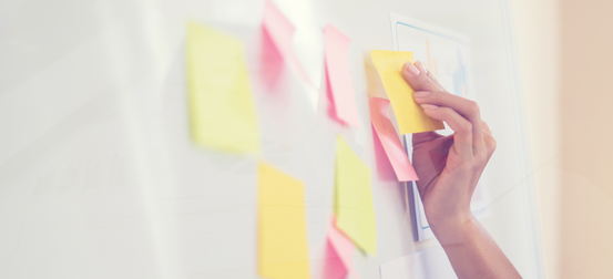 A woman is writing on a whiteboard with sticky notes