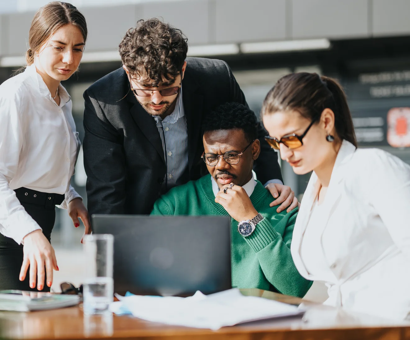 Group of professionals gathered around a laptop, discussing work outdoors