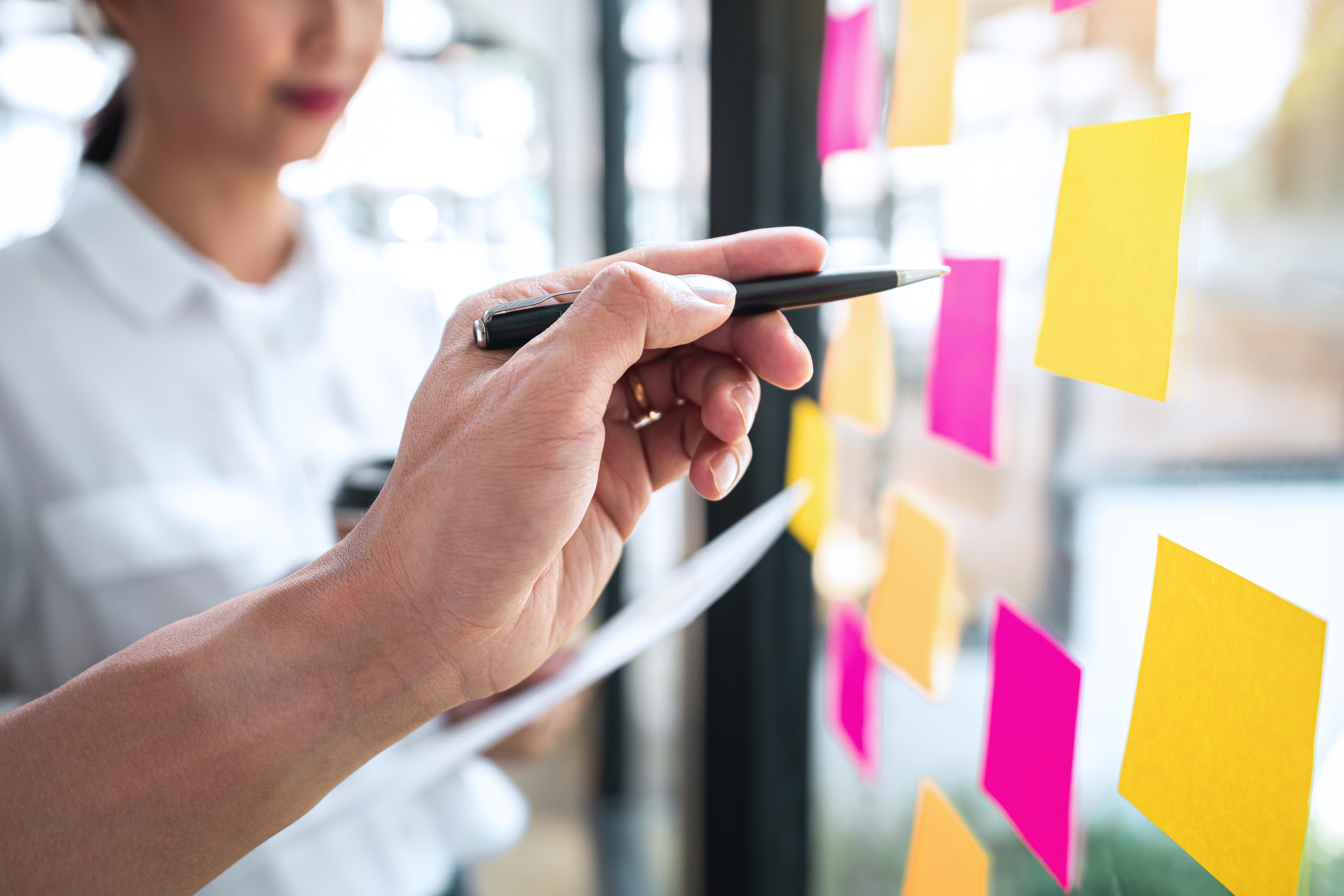 A person is writing on a glass wall with sticky notes