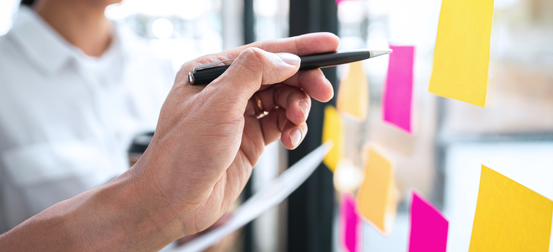 A person is writing on a glass wall with sticky notes