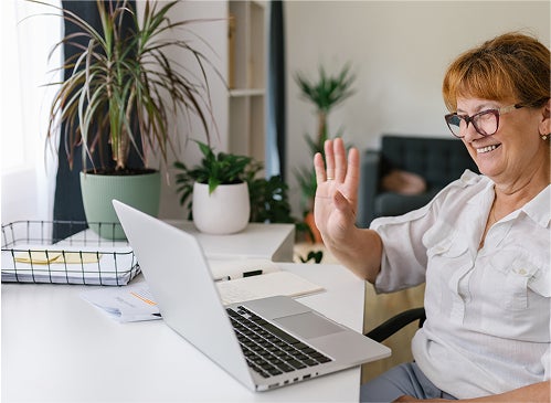 An older woman waving during a video call.