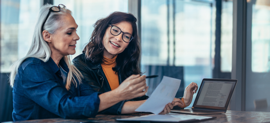 Two women are sitting at a table looking at a piece of paper