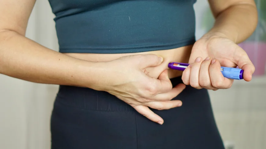A diabetes patient is injecting herself with a syringe in her stomach
