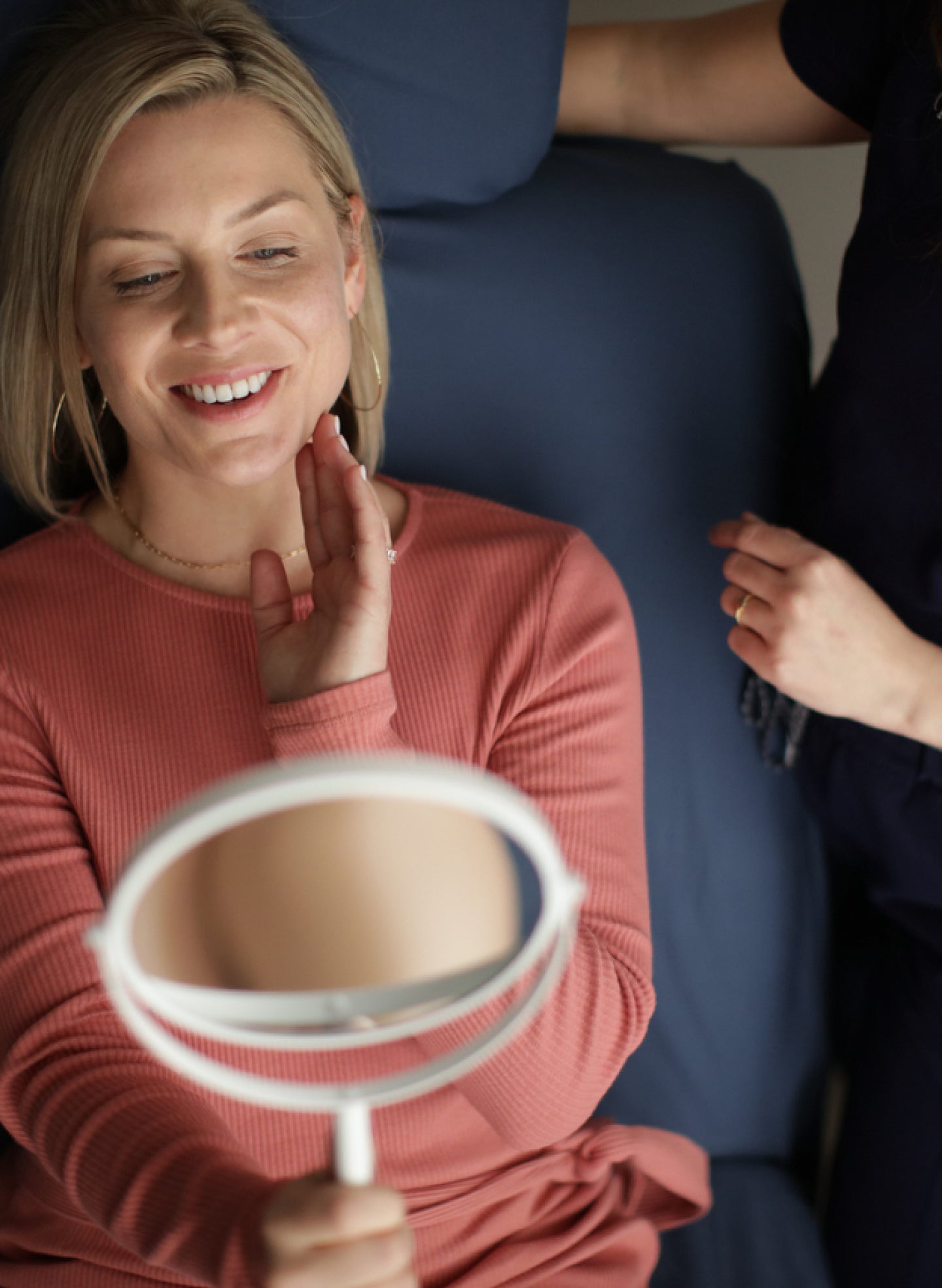 A woman is looking at her face in a mirror.