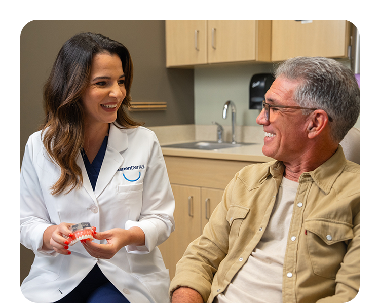 Smiling dental expert from Aspen Dental shows implant model while helping patient understand financing options.