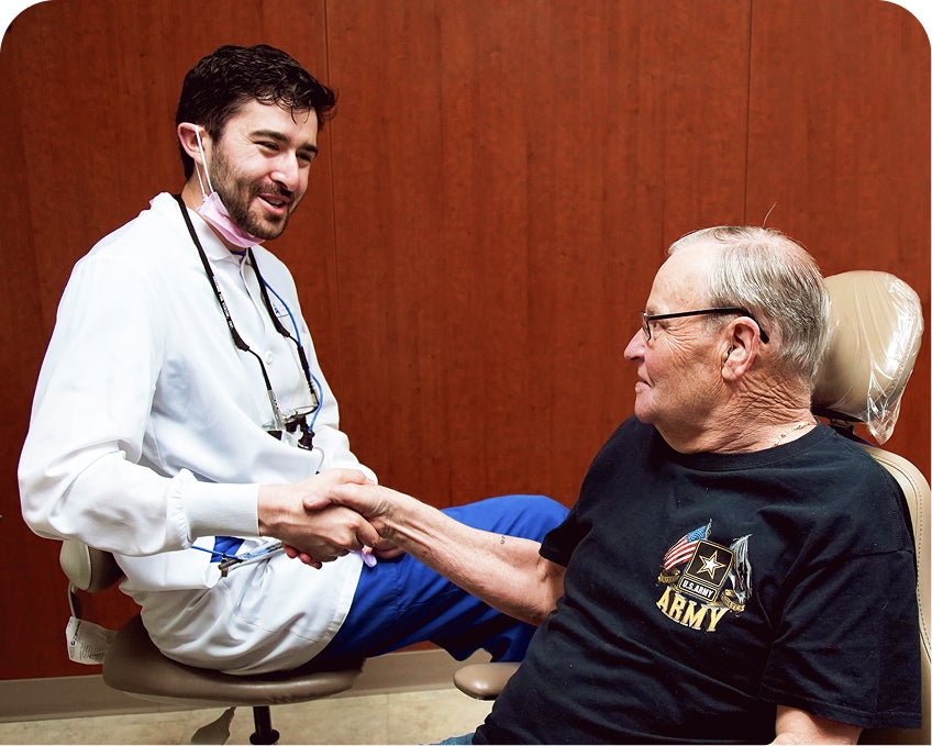 A smiling Aspen Dental professional shakes hands with a veteran patient wearing an Army shirt, celebrating enrollment in the Aspen Dental Savings Plan and highlighting satisfaction, savings, and veteran dental care support.