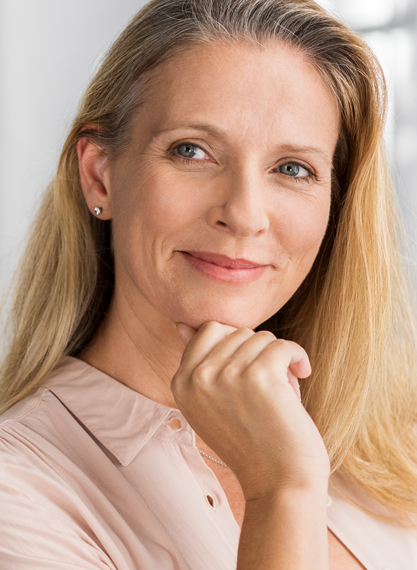 A woman with long blonde hair smiles at the camera, her chin resting on her hand