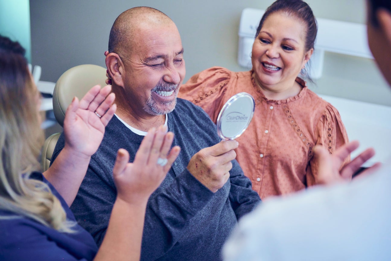 ClearChoice patient celebrating their new smile after dental implant surgery, accompanied by a dental professional and family member, highlighting affordable implant options.