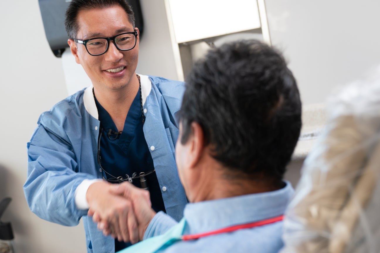 A ClearChoice dentist in professional attire warmly shaking hands with a patient during a consultation, showcasing a commitment to personalized dental implant care and patient trust.