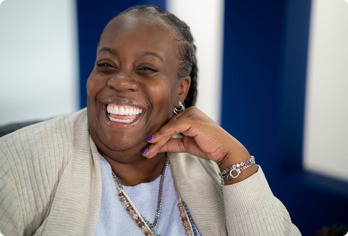 A women wearing a beige cardigan smiling confidently at the camera with her new dental implants.