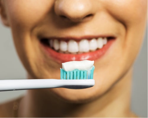  Close-up of a bright smile with a toothbrush, promoting good oral hygiene practices recommended by Aspen Dental.
