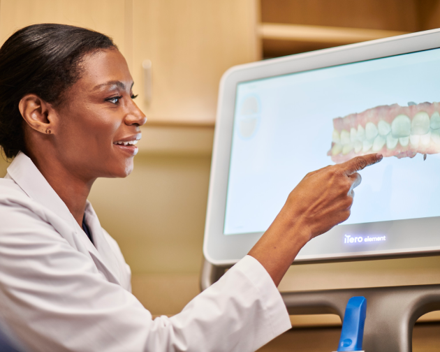 A dentist pointing at a digital screen displaying a dental treatment plan, showcasing advanced technology for planning tooth cap procedures at Aspen Dental.