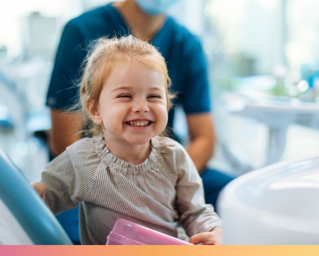 A young child smiling happily while sitting in a dental chair at the dentist's office, conveying a positive dental experience, used by Motto.