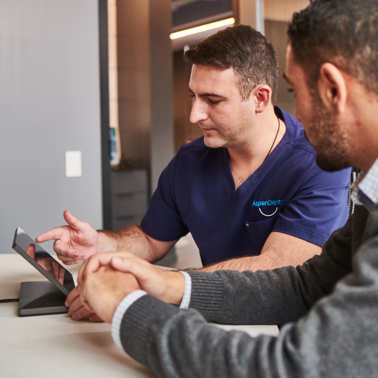 Dentist at Aspen Dental showing a patient treatment options on a tablet, focusing on solutions for front tooth implants in a modern, professional setting.