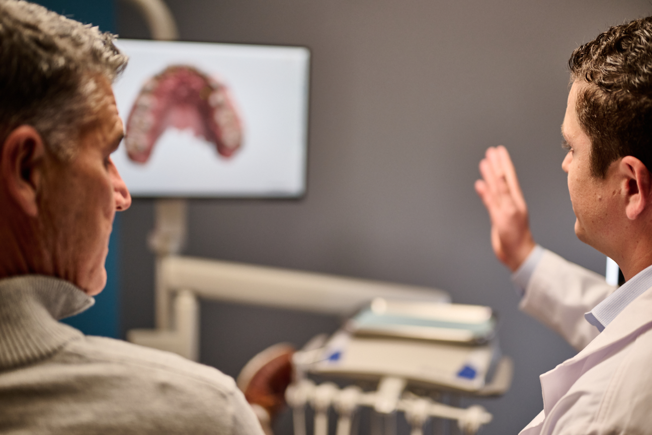 A dentist at Aspen Dental discussing a digital dental scan displayed on a screen with a male patient in a modern clinic setting.