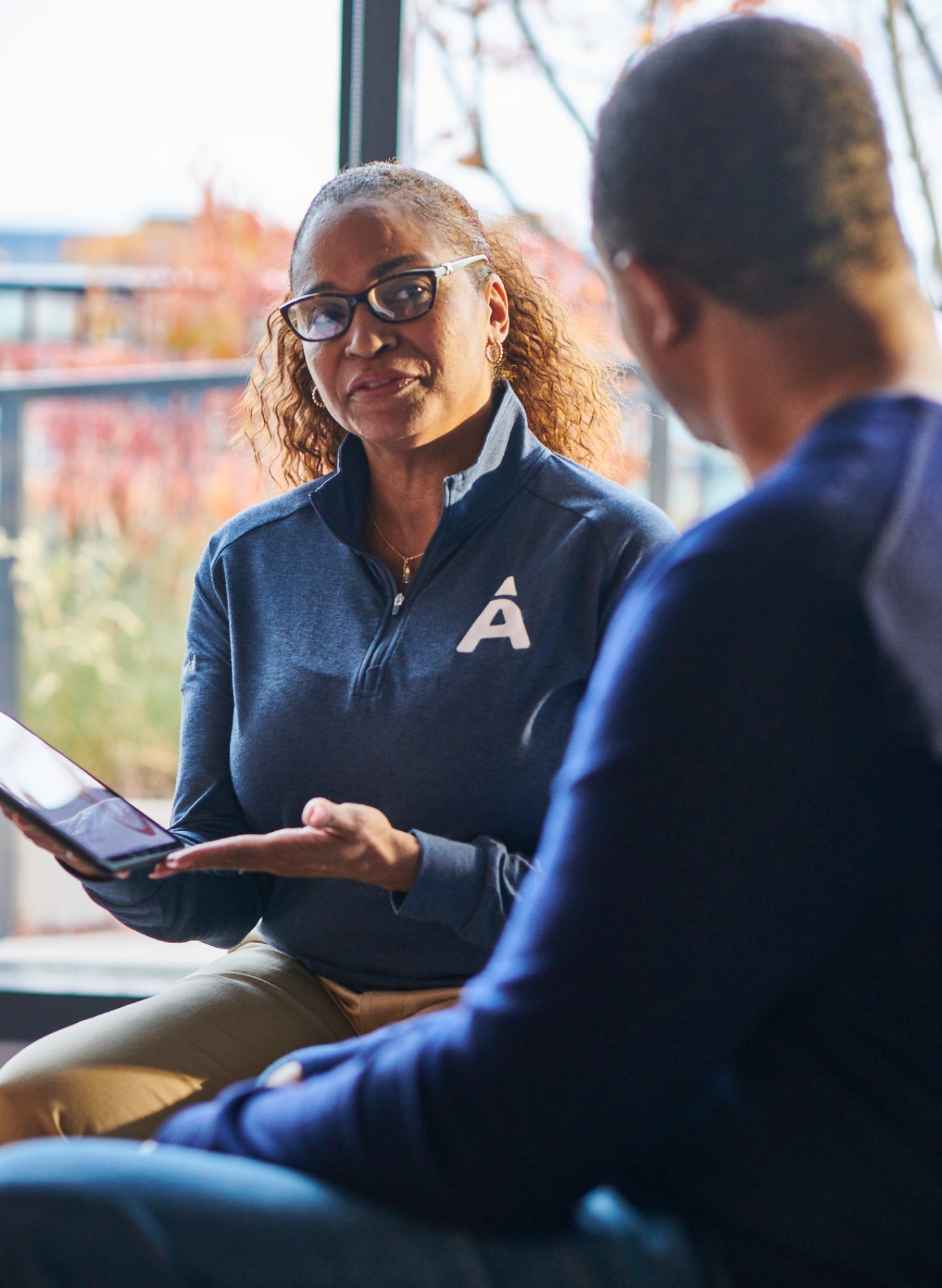 A professional from Aspen Dental explains wisdom tooth infection symptoms and treatment options to a patient, using a tablet for visual aid in a modern office setting.