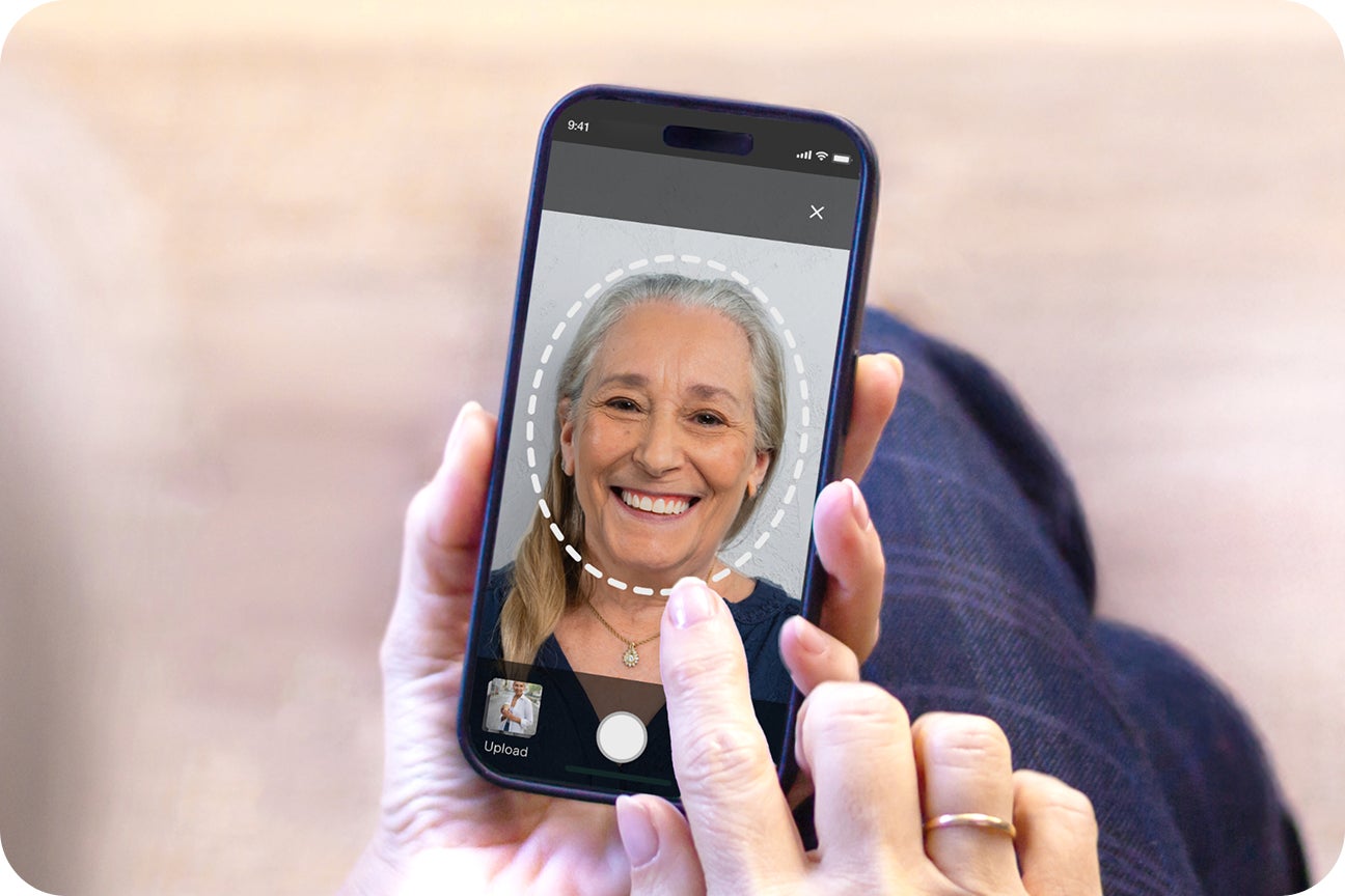 A patient holds a smartphone to take a selfie of themselves to use within Aspen Dental's smile try-on mobile simulator tool to see what their smile could look like with dental care services and treatment.
