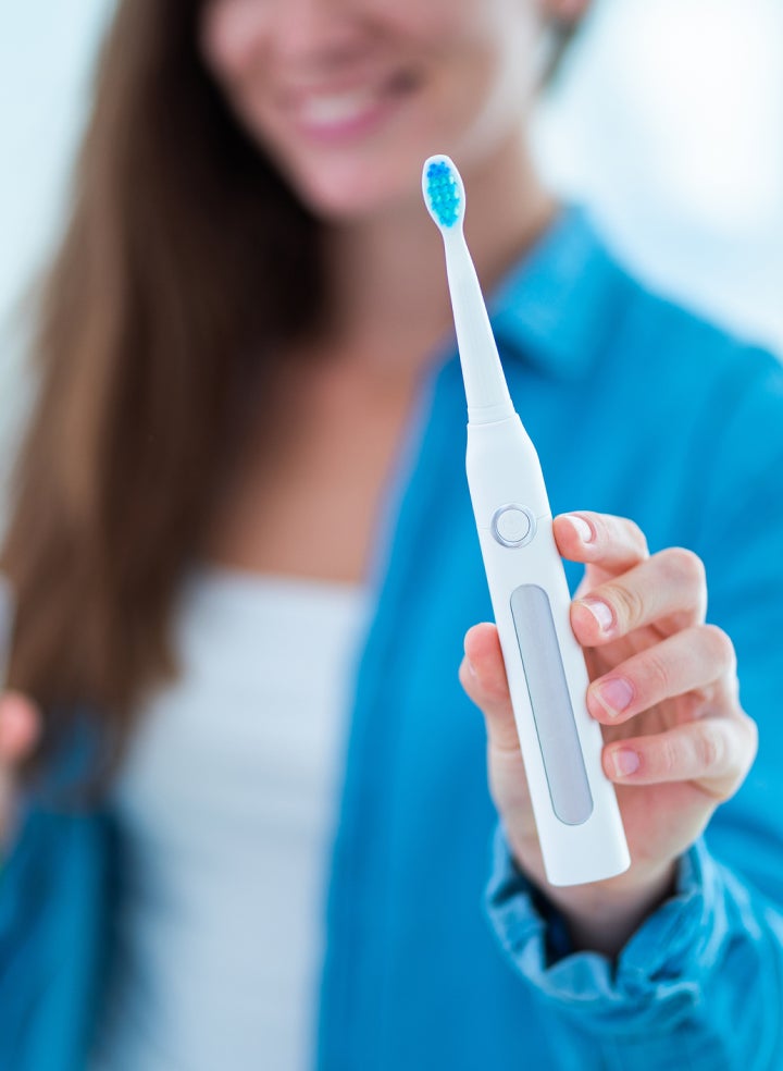 A woman in a blue jacket is holding an electric toothbrush