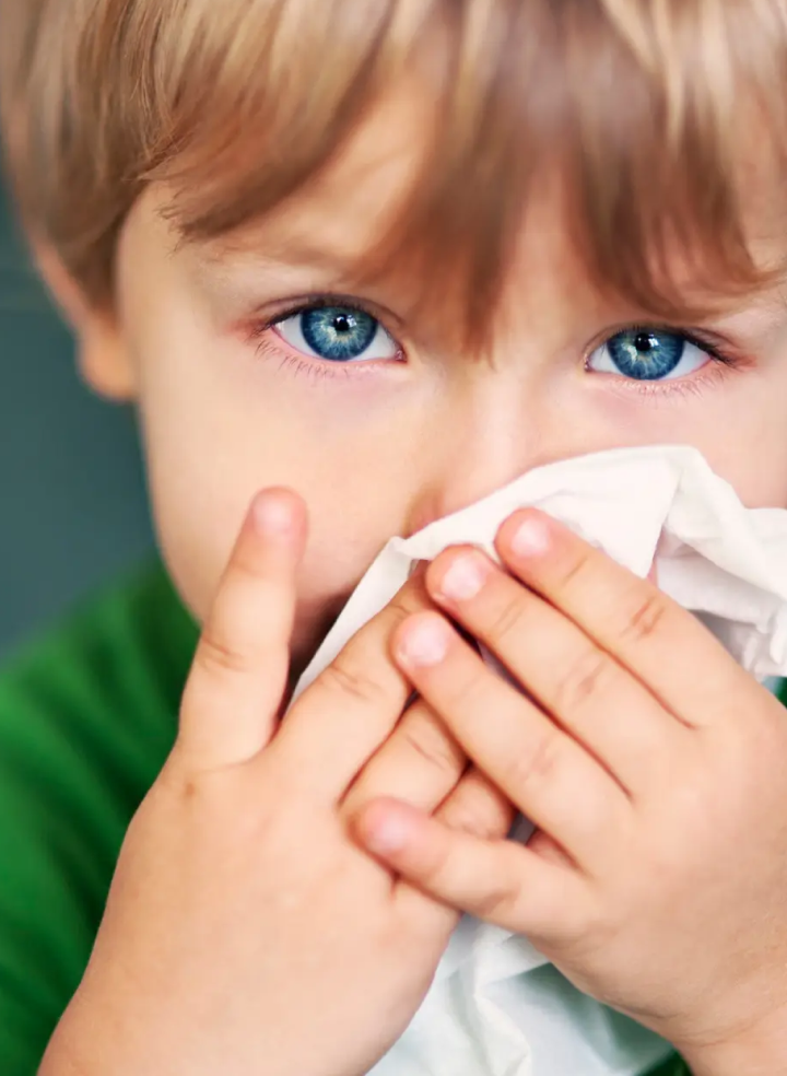 A young boy blowing his nose into a napkin.