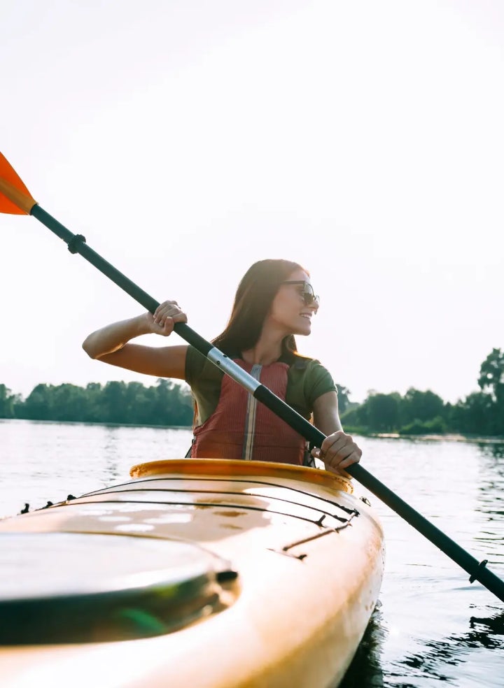 A woman is paddling a yellow kayak on a lake