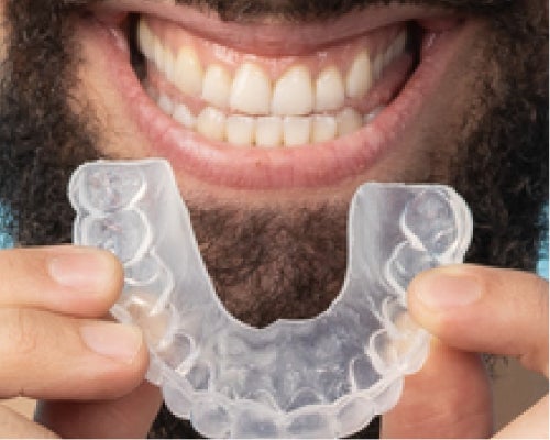 Close-up of a person holding a clear aligner and smiling, highlighting orthodontic solutions available at Aspen Dental.