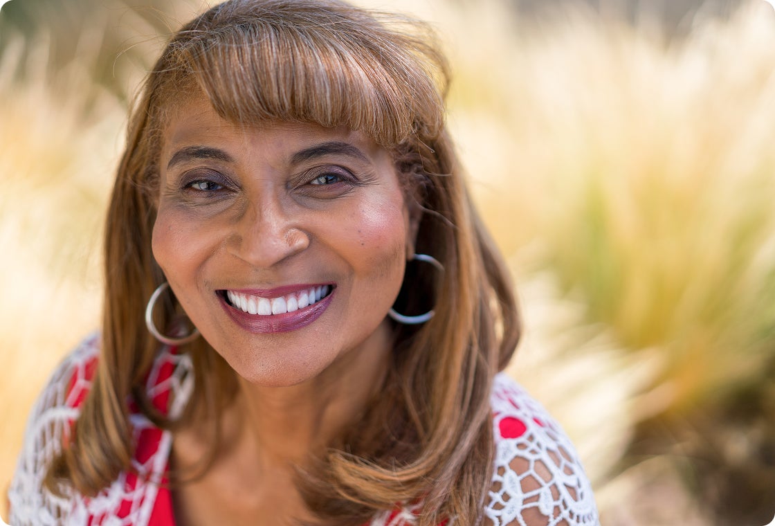 A smiling woman in a white hollow out shirt enjoying the outdoors with her new dental implants.