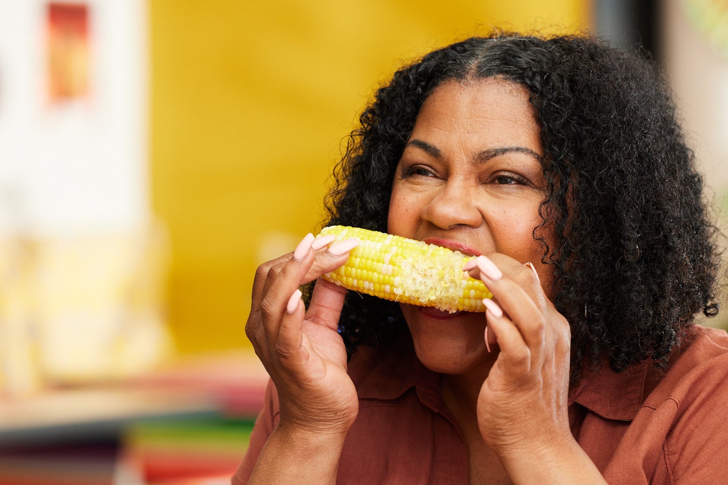 A smiling woman confidently biting into a corn on the cob, showcasing the benefits of restored dental health through Aspen Dental care.