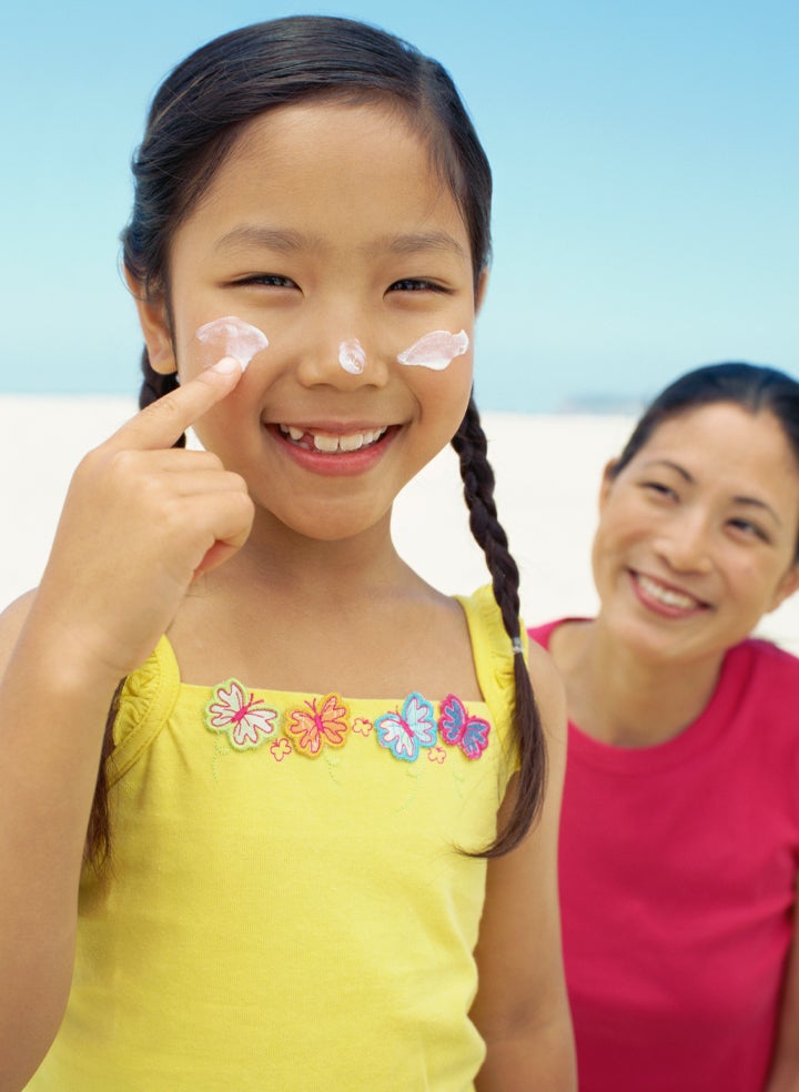 A little girl is applying sunscreen to her face