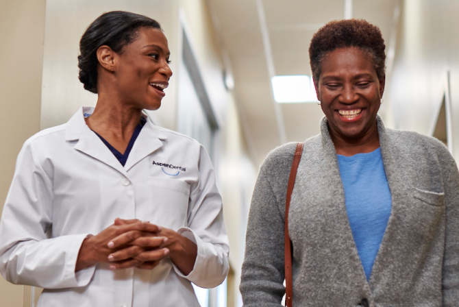 A smiling patient walking alongside a dentist in the hallway, representing compassionate care and expert guidance for tooth cap solutions at Aspen Dental.
