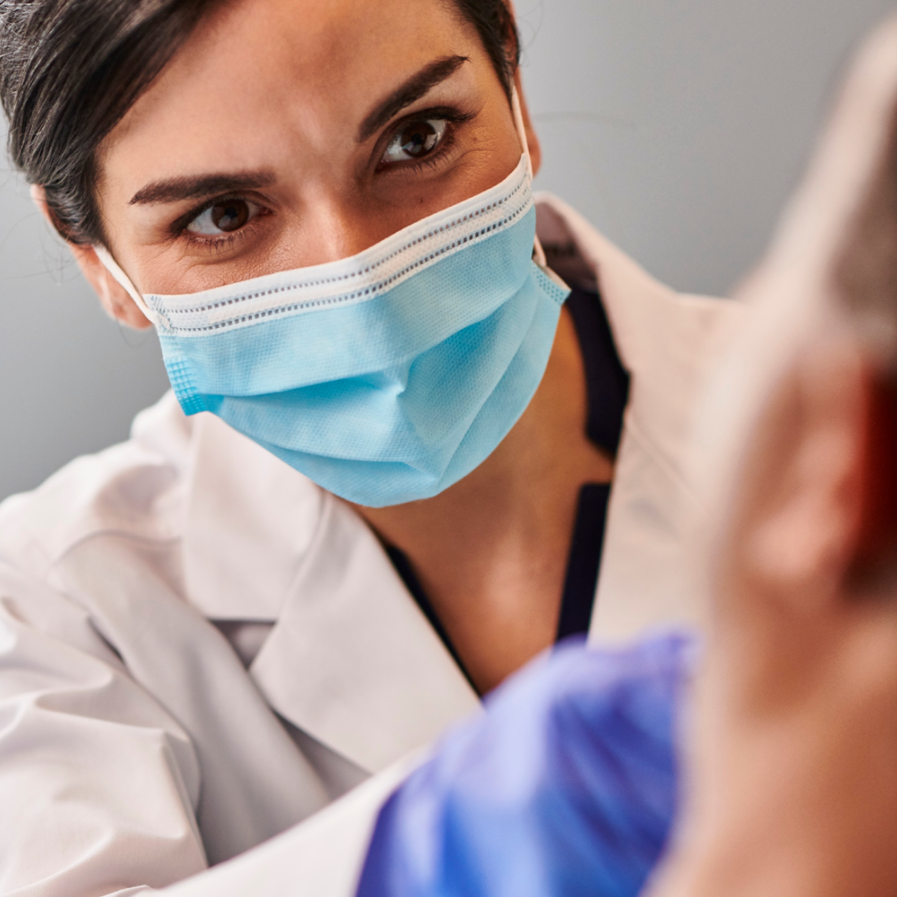 Close-up of a dentist in a protective mask carefully examining a patient, emphasizing expertise in front tooth implant procedures at Aspen Dental.