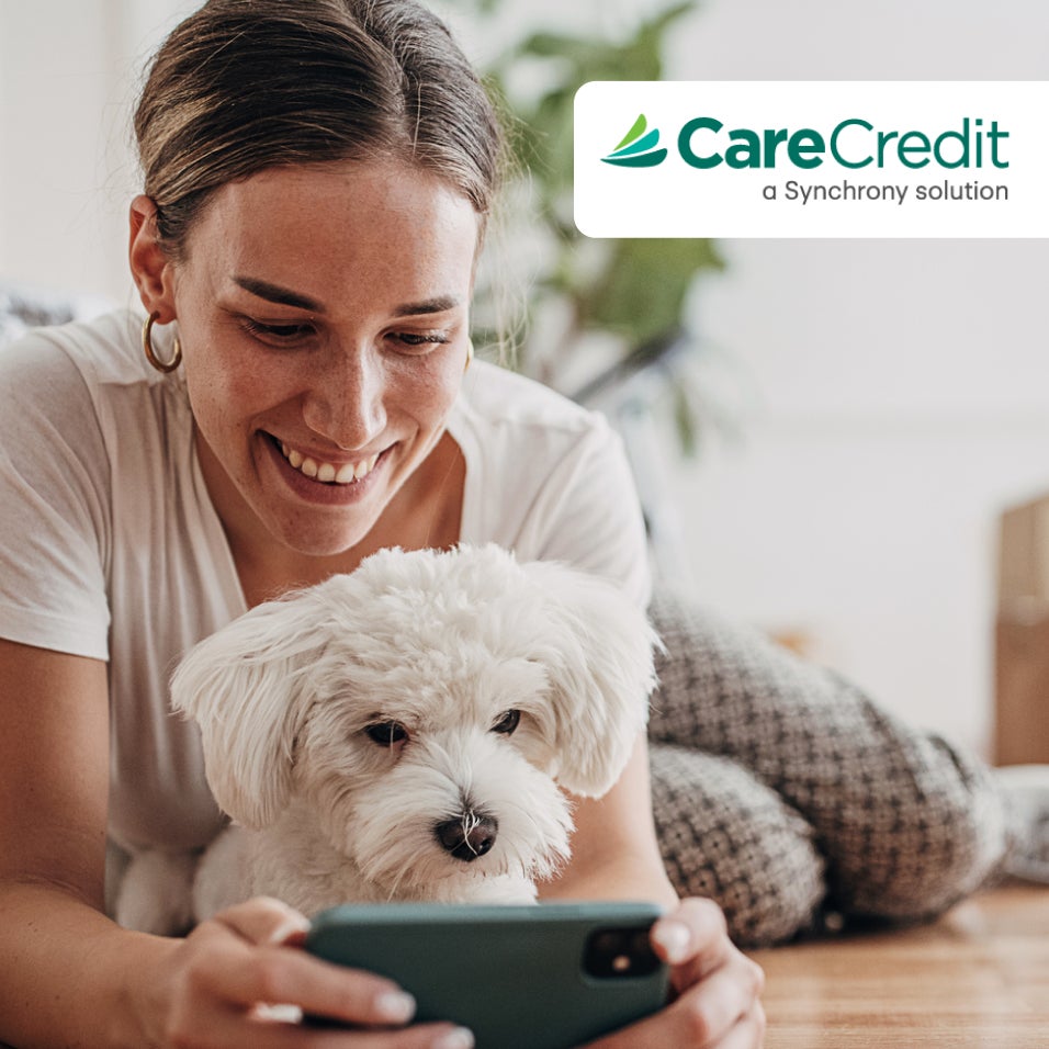 CareCredit graphic with woman smiling holding her dog and smartphone.