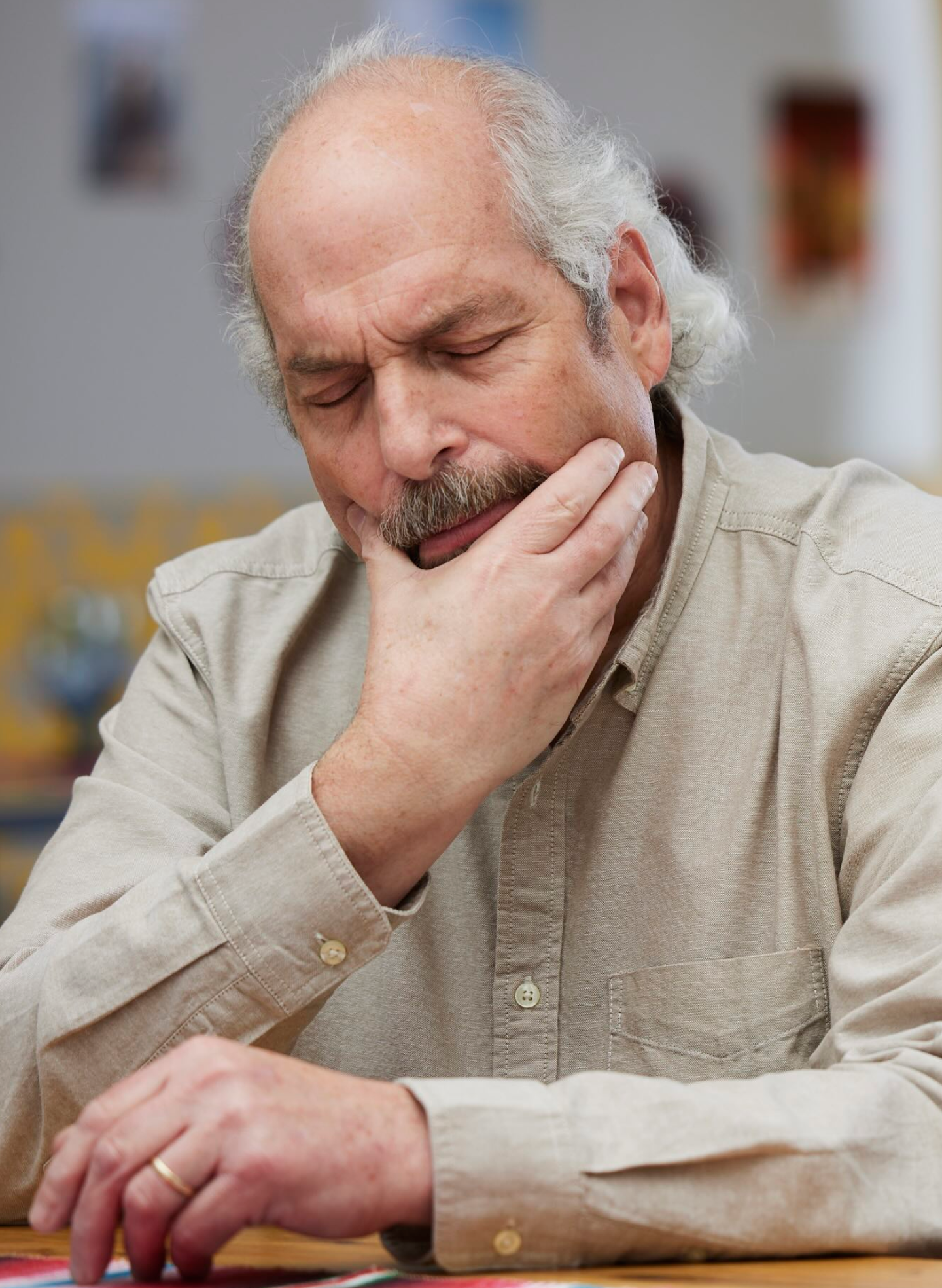 Elderly man with a pained expression holding his jaw, indicating difficulty in removing dentures.