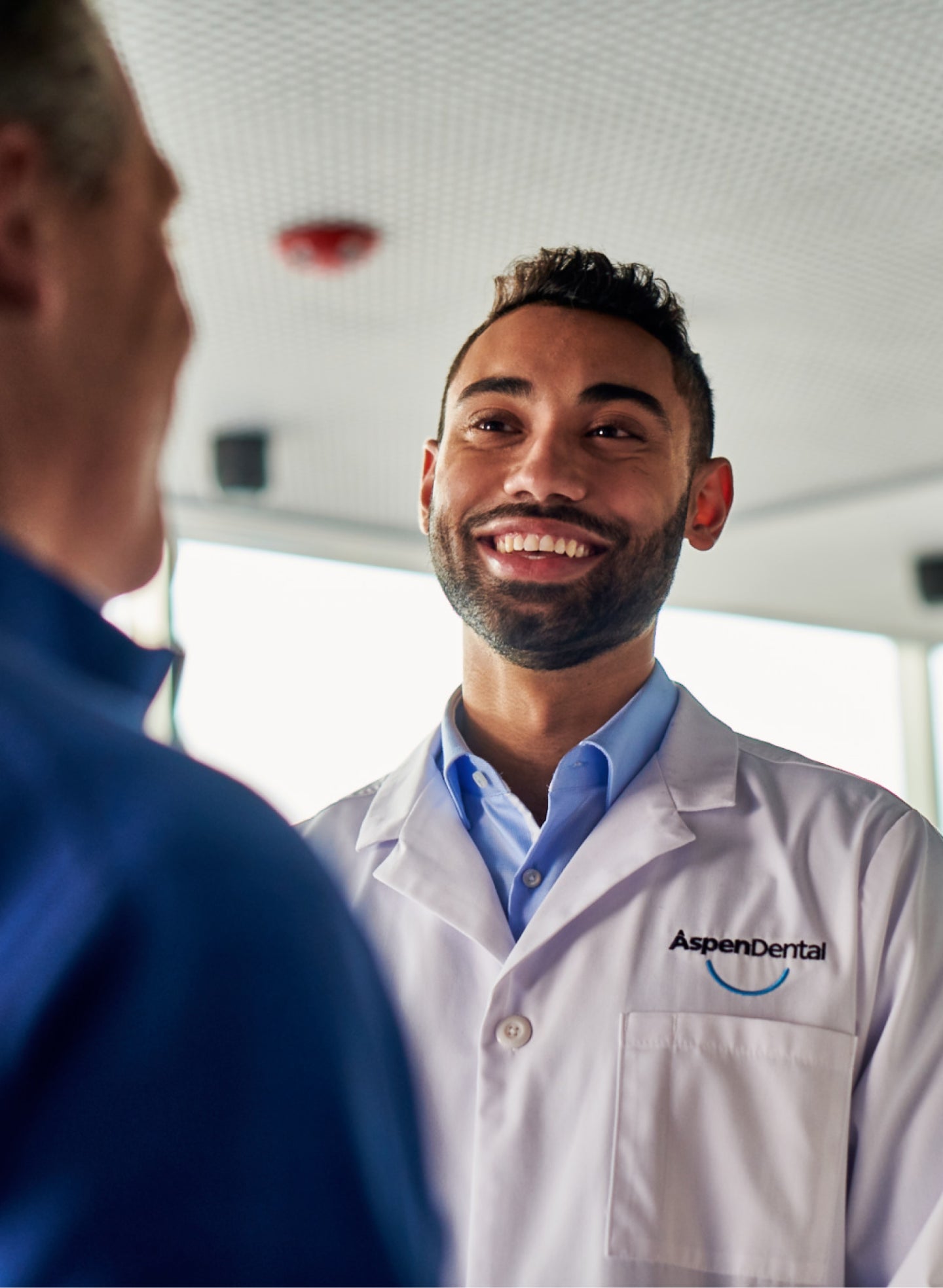 A smiling dentist in an Aspen Dental coat speaking with a patient, discussing the factors influencing how long a root canal can last with proper care.