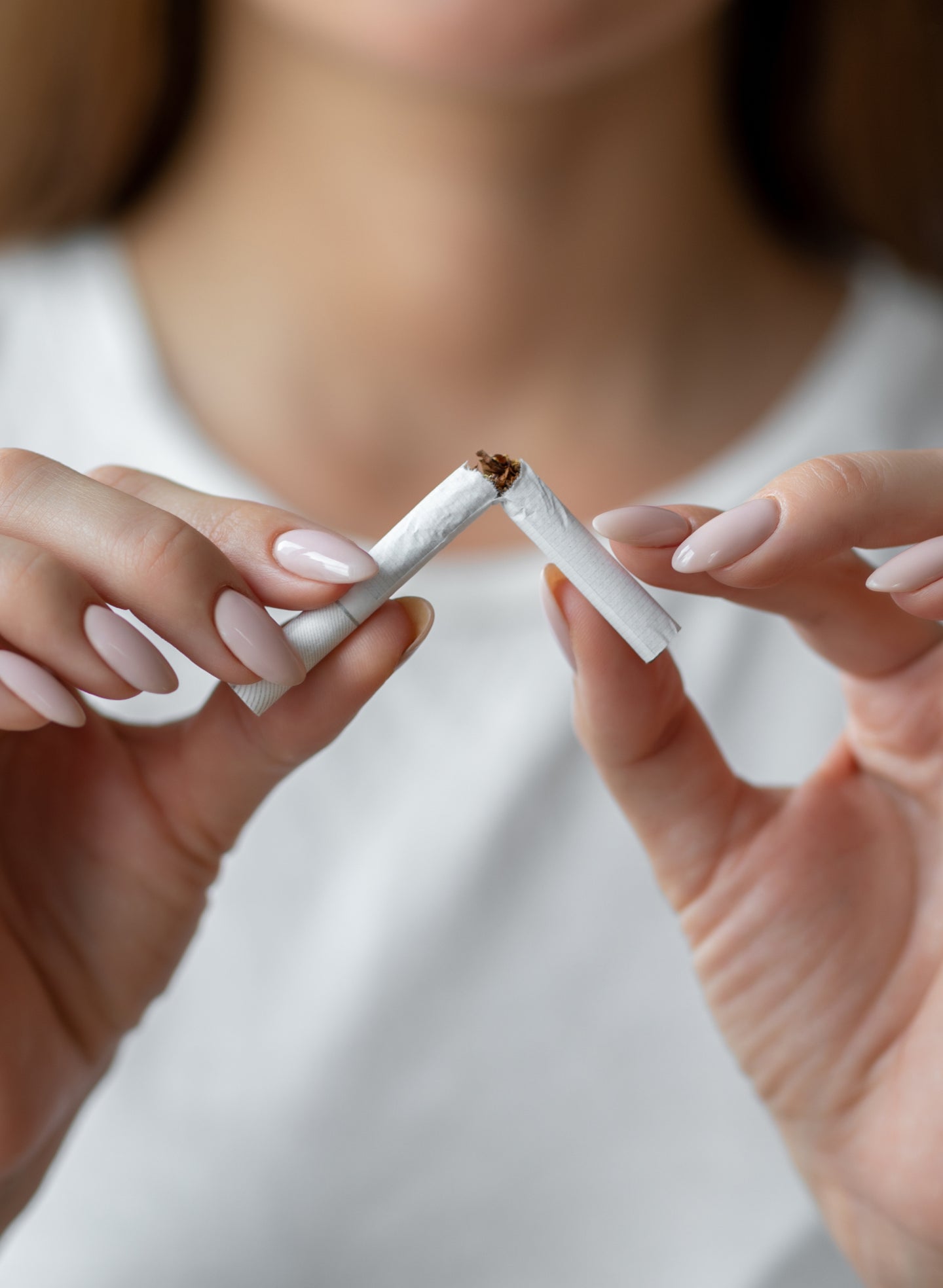 A woman breaks a cigarette in half with both hands, symbolizing the decision to quit smoking. This visual connects to oral health and reducing risks of smoking with dental implants.
