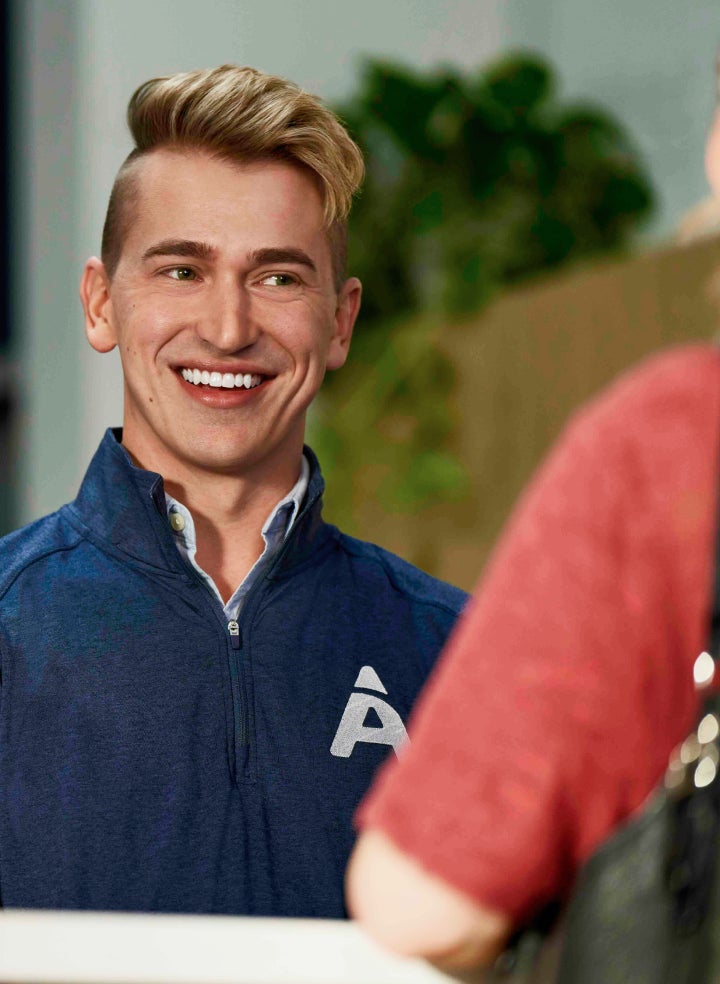 A friendly Aspen Dental staff member smiling while engaging with a patient, emphasizing the importance of avoiding smoking after a dental procedure to prevent complications and ensure healing.
