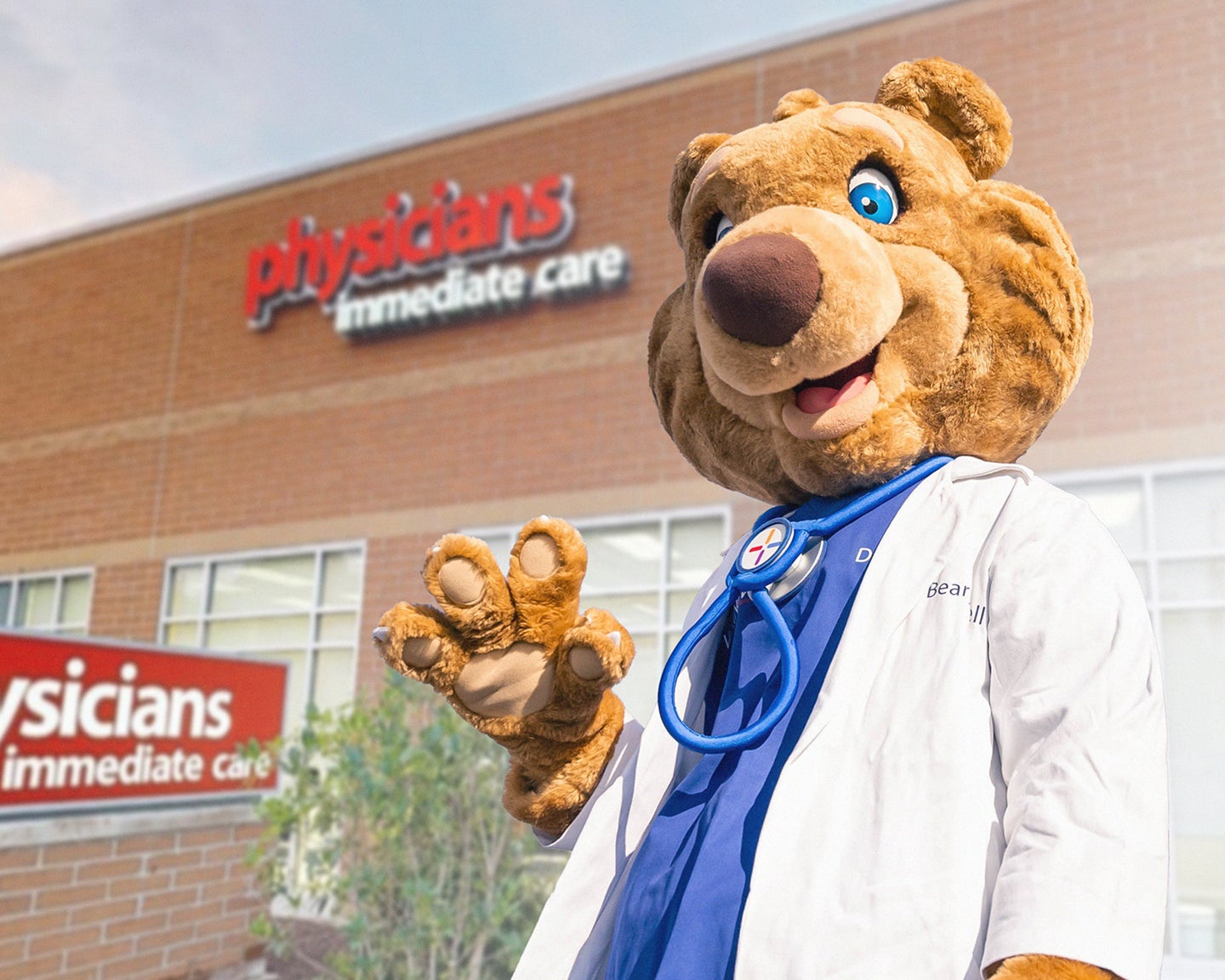 The WellNow mascot Doctor Bearywell in front of a Physicians Immediate Care clinic.