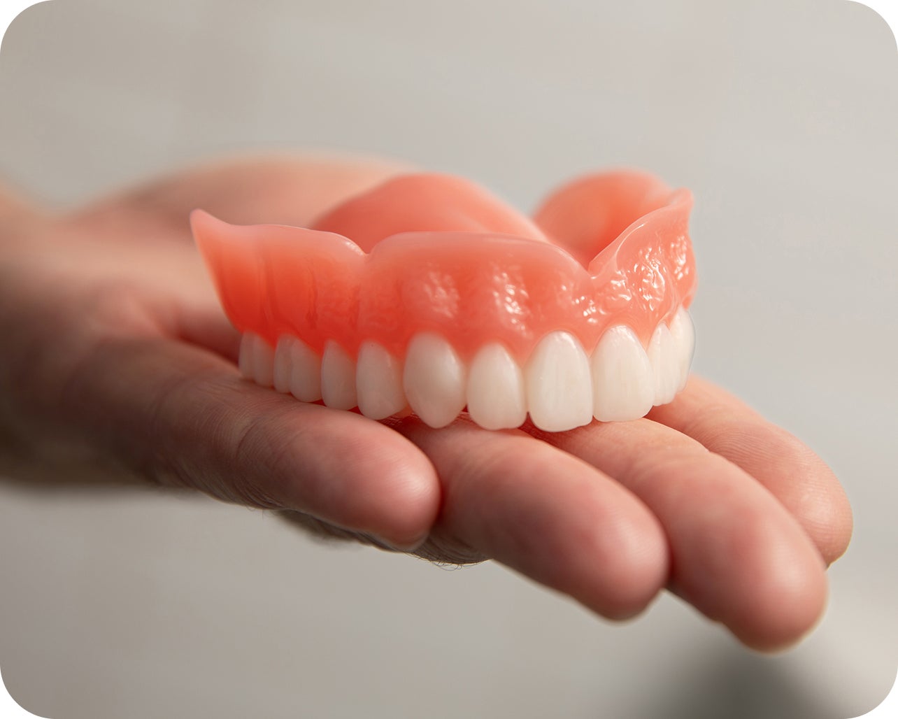 A close up of a denture sitting on a dentist's hand to highlight the different types of denture solutions available at Aspen Dental and promotes patients to compare denture options.