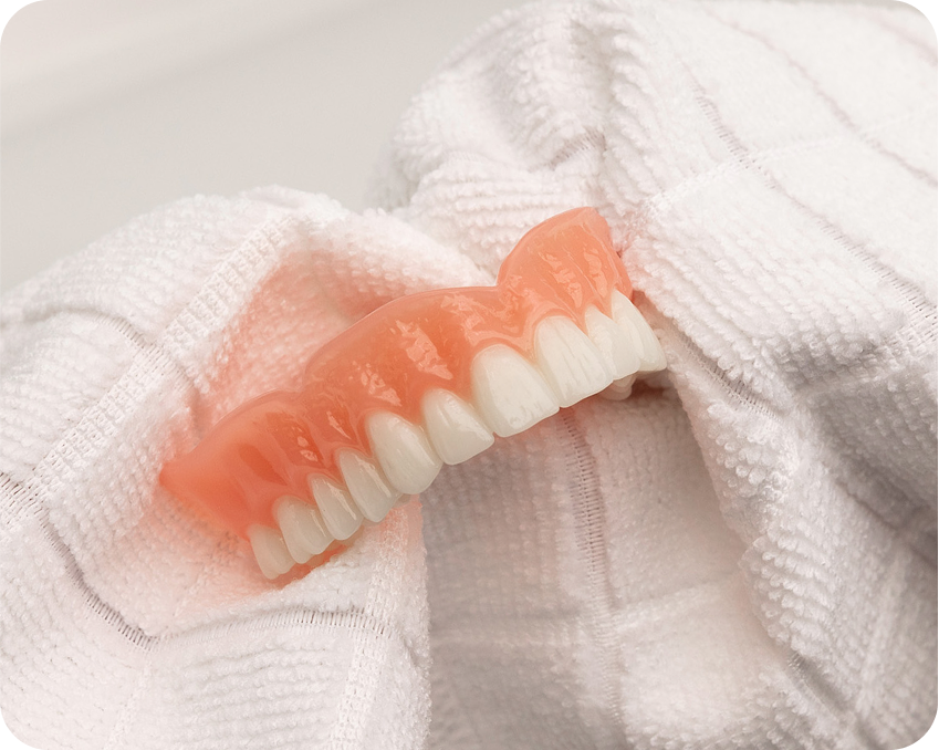 Drying a clean denture with a towel before applying adhesive – Aspen Dental denture care step.