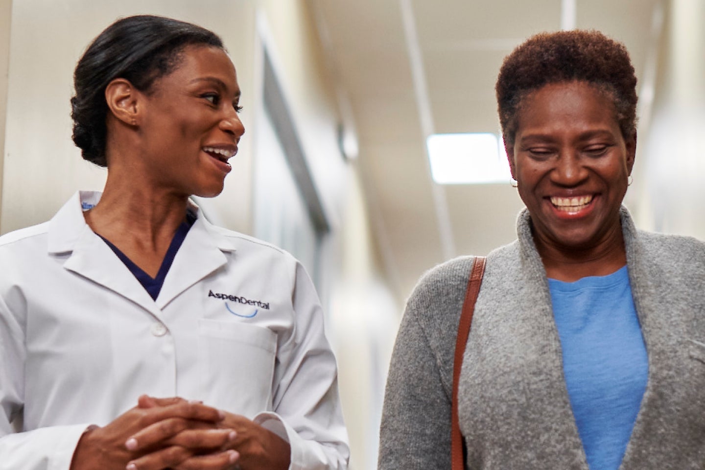 A smiling patient walking alongside an Aspen Dental professional, highlighting a positive and comfortable dental care experience.