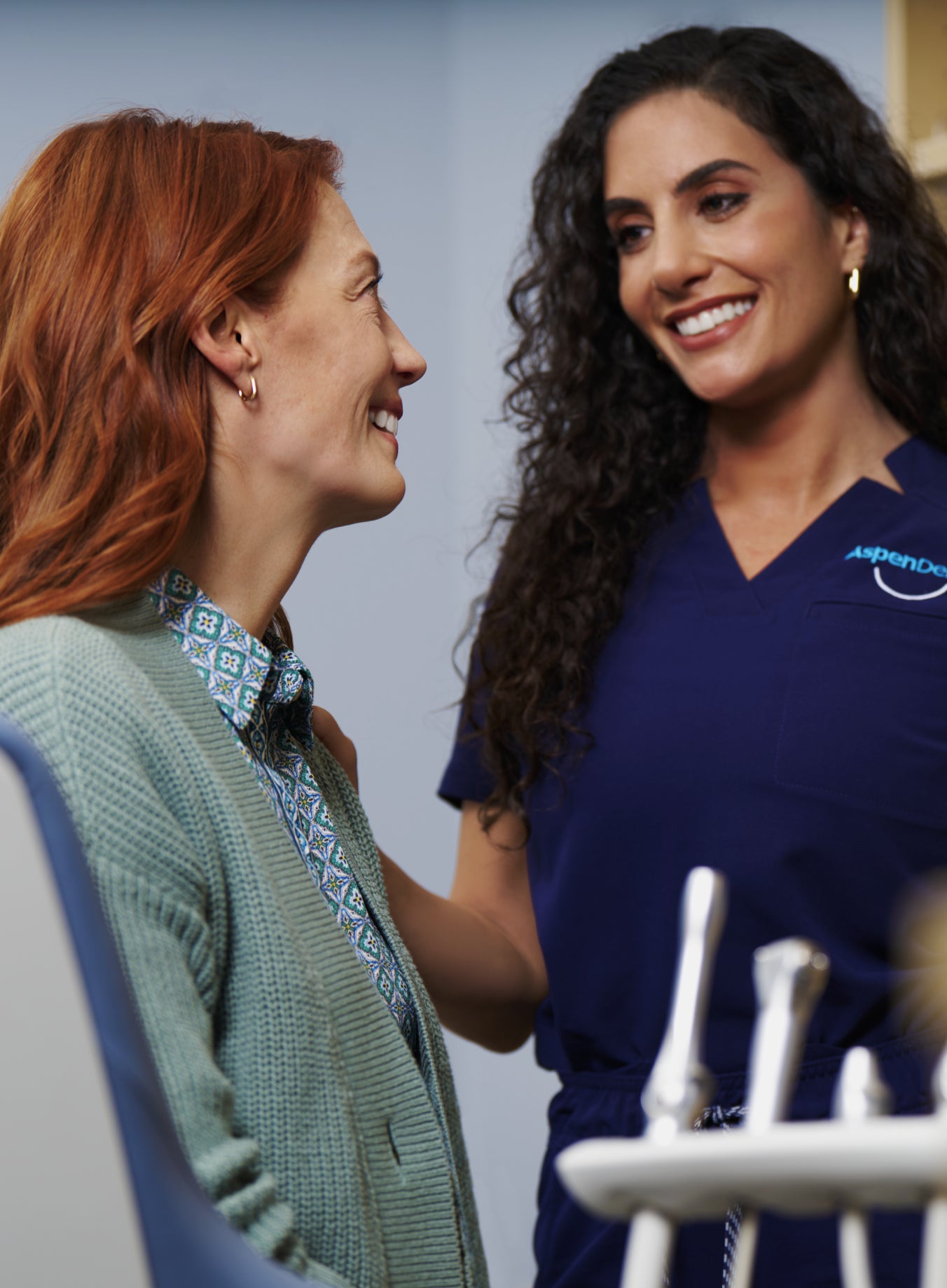 A woman reclines in a dental chair, smiling confidently post-treatment. Dental tools are visible in the background.