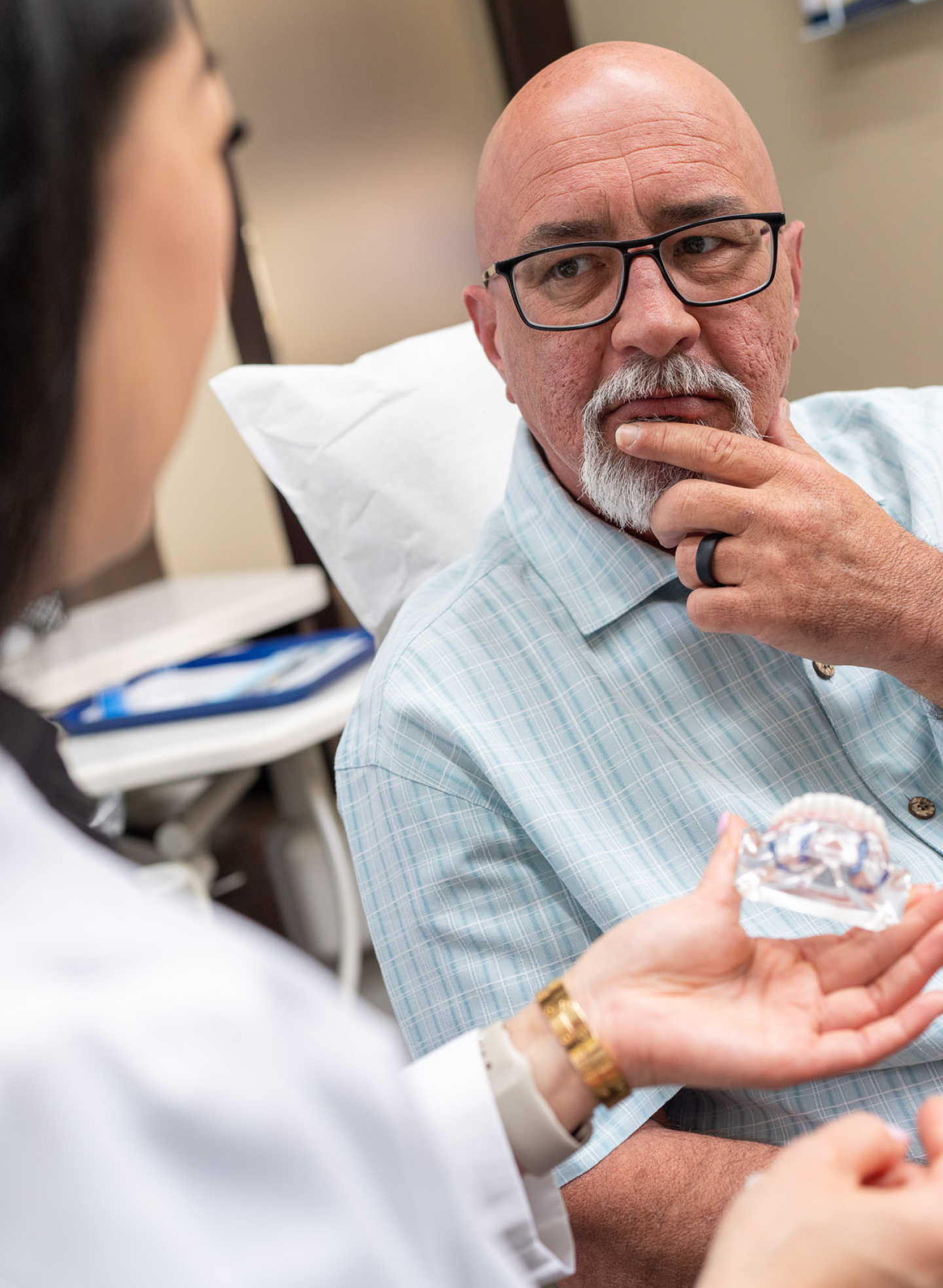 A ClearChoice patient listens attentively during a consultation as a dental professional explains the features of dental implant crowns using a model.